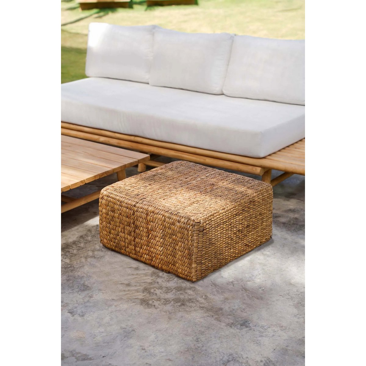 Pouf carré tressé en fibres naturelles – vue trois quarts, rideaux lin blanc