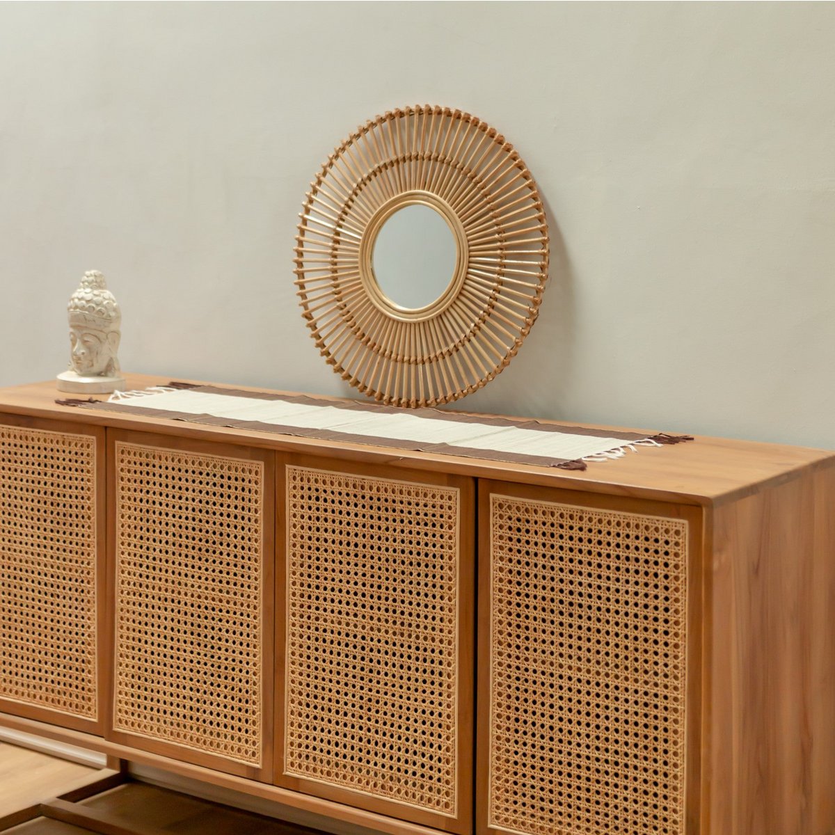 Miroir BUMI en rotin naturel posé sur un buffet en bois avec décoration bohème