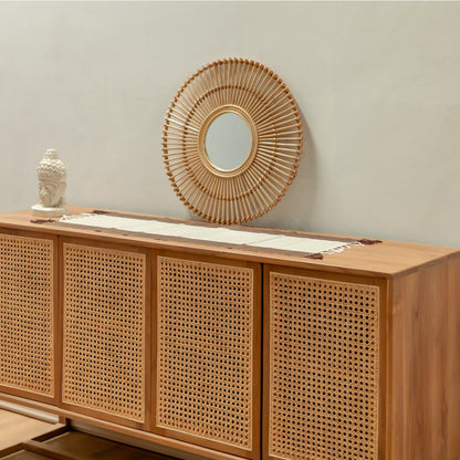 Miroir BUMI en rotin naturel posé sur un buffet en bois avec décoration bohème